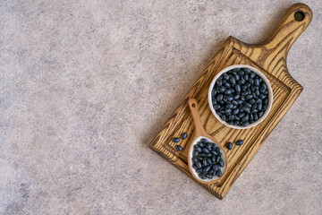 Black beans in ceramic bowl and spoon on wooden board. Top view