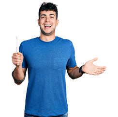 Young hispanic man holding electric toothbrush celebrating achievement with happy smile and winner...