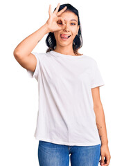 Fototapeta premium Young woman wearing casual clothes doing ok gesture like binoculars sticking tongue out, eyes looking through fingers. crazy expression.