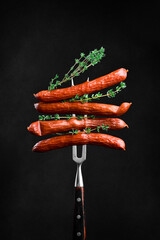 Traditional Bavarian sausages with thyme on a fork. Barbecue with sausages. On a black background.
