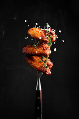 Fork with baked chicken wings, salt and smoke in the photo. Traditional Buffalo Chicken Wings.