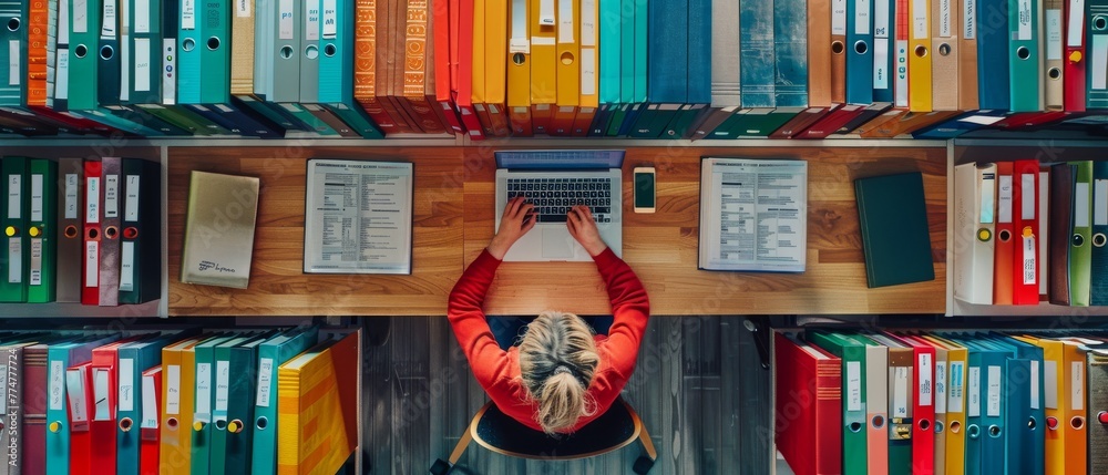 Poster Top view of an archive with ring binders and a woman searching for files on a laptop, surrounded by binders
