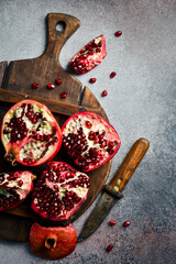 A wooden kitchen cutting board with a piece of fresh pomegranate. On a concrete background.