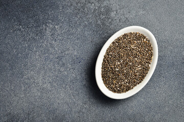 Close up of chia seeds in a ceramic bowl. Superfood On a dark concrete background. - obrazy, fototapety, plakaty