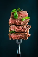Foto op Aluminium Slices of ribeye steak on a metal fork. Roast medium rare. On a black background. © Yaruniv-Studio