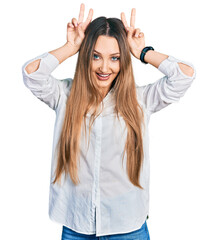Beautiful caucasian woman wearing casual white shirt posing funny and crazy with fingers on head as bunny ears, smiling cheerful