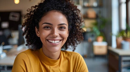 A smiling woman with glasses using a laptop in a lively workspace.