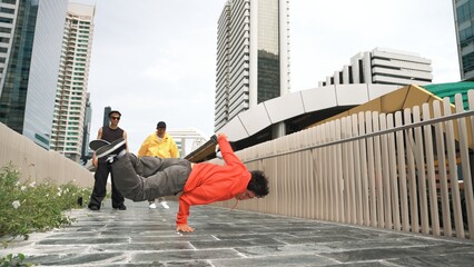 Professional hipster doing head spin while multicultural friend cheering him. Street dancer looking at camera while pose at camera. Freestyle dancing. Modern lifestyle. Outdoor sport 2024. Sprightly.