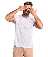 Young hispanic man wearing casual clothes and glasses covering eyes with hands smiling cheerful and funny. blind concept.