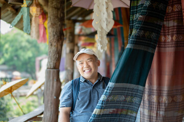 Asian middle-aged man in white cap and t-shirt  smiling  and holding woven fabric which hanging and...