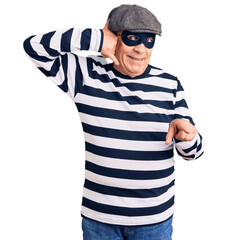 Senior handsome man wearing burglar mask and t-shirt smiling doing talking on the telephone gesture...