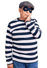 Senior handsome man wearing burglar mask and t-shirt thinking looking tired and bored with...