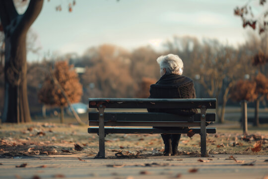 An elderly woman sits alone on a park bench, melancholy of social isolation and loneliness.
