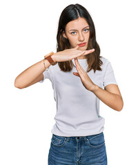 Young beautiful woman wearing casual white t shirt doing time out gesture with hands, frustrated...