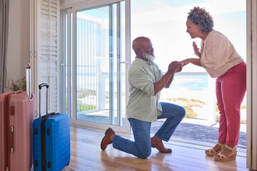 Mature Couple With Man Proposing Marriage Kneeling And Giving Woman Ring In Beach Front Property - Powered by Adobe