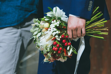 groom holding delicate white and green wedding bouquet with red berries