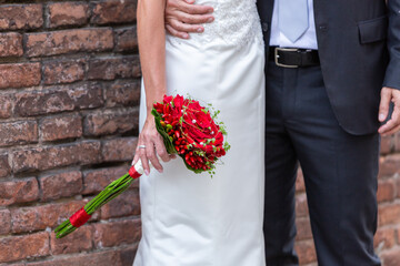 bride and groom holding hands with vibrant bouquet against brick wall