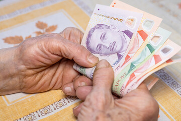 Hands of an elderly woman hold several Singapore dollars in their hands, Economic concept, Home budgets of pensioners in Singapore, rising cost of living and expenses - 774808921