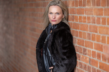 Portrait of a beautiful young blonde woman in a black coat on a brick wall background
