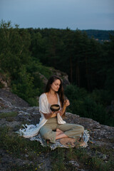 Young woman meditating using a tibetan singing bowl while sitting in a mountain landscape.