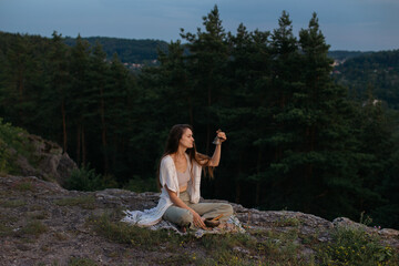 A young woman meditating with a Gantha Buddhist bell in her hands, sitting on a rock in the rays of the setting sun.