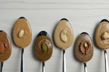 Foto op Plexiglas Tasty nut butters in spoons and raw nuts on white wooden table, flat lay. Space for text © New Africa