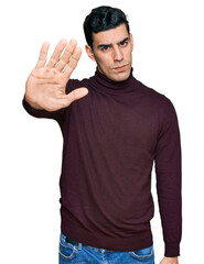 Fototapeta premium Handsome hispanic man wearing casual turtleneck sweater doing stop sing with palm of the hand. warning expression with negative and serious gesture on the face.