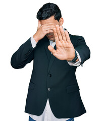 Handsome hispanic man wearing business clothes covering eyes with hands and doing stop gesture with sad and fear expression. embarrassed and negative concept.