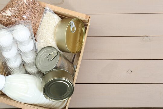 Donation box with food products on wooden table, top view. Space for text