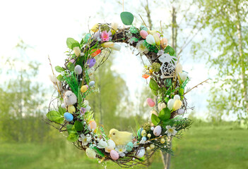 beautiful decorative Spring wreath hanging in garden, green natural background. symbol of Easter...