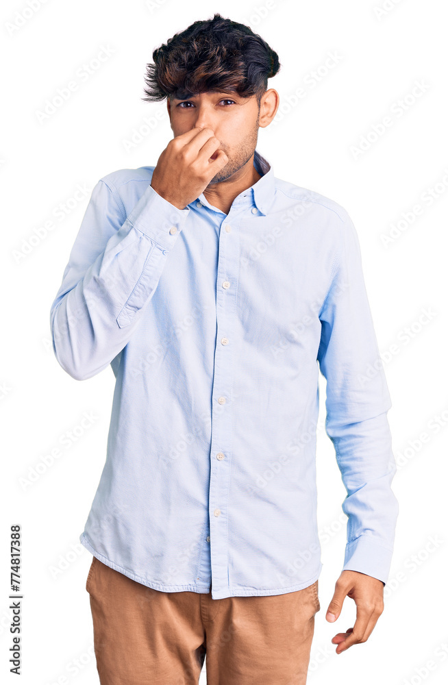 Wall mural Young hispanic man wearing casual shirt smelling something stinky and disgusting, intolerable smell, holding breath with fingers on nose. bad smell