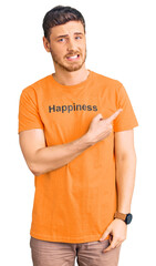 Handsome young man with bear wearing tshirt with happiness word message pointing aside worried and...