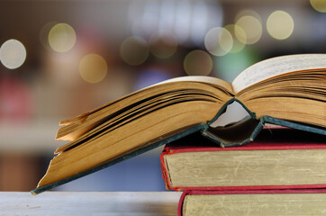 Stack of books and open book, blurred bookshelf background with bokeh balls, reading, learning,...