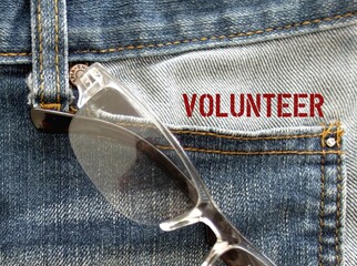 Reading glasses and text on jeans pocket VOLUNTEER, a person who does something or helping others...