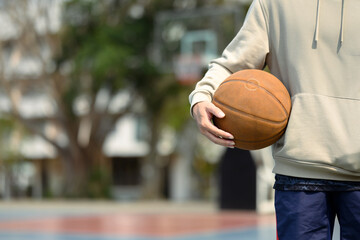 Teenage man holding a ball standing on the basketball court. Sport and active lifestyle concept
