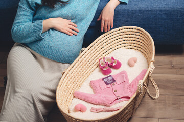 Happy mother enjoying pregnancy. Wicker basket of cute tiny stuff newborn. Beautiful pregnant woman at home.