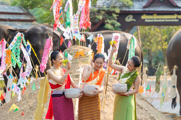 Songkran festival. Northern Thai people in Traditional clothes dressing splashing water together in Songkran day cultural festival with sand pagoda and colorful paper flag.