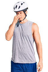 Young handsome man wearing bike helmet smelling something stinky and disgusting, intolerable smell, holding breath with fingers on nose. bad smell