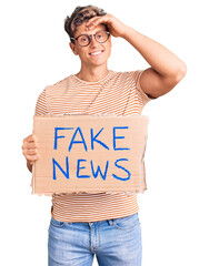 Young handsome man holding fake news banner stressed and frustrated with hand on head, surprised...