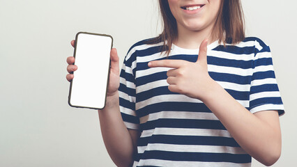 Happy boy showing to camera and pointing at empty free space. Background with free space, mockup. Young guy holding smartphone.