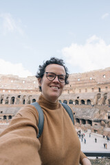 A woman is taking a selfie in the Colosseum, she is smiling and look at camera