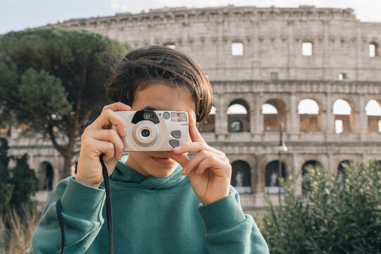 A girl in green sweater taking pictures with an old film camera, outside the Roman colosseum