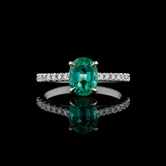 Beautiful white gold ring with diamonds and emerald on a black background