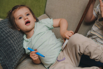 Portrait of small caucasian girl lying on the sofa holding blue felt pen. Childhood leisure fun play learning development concept