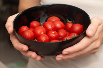 Cherry Tomatoes in a bowl in female hands. Hands cradling a black bowl filled with bright red cherry tomatoes.