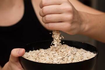 Oats Trickling from Hand into Bowl. Hand sprinkling rolled oats into a black bowl.