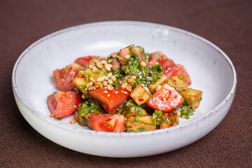 Fresh tomato and avocado salad with pine nuts and herbs on a white plate
