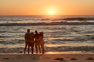 Rear View Silhouette Of Mature Couple With Friends On Beach Looking Out To Sea At Sunset