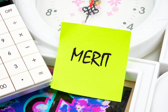 Business and merit concept. MERIT written on a yellow sticker near the calculator and the clock