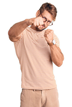 Young caucasian man wearing casual clothes and glasses punching fist to fight, aggressive and angry attack, threat and violence